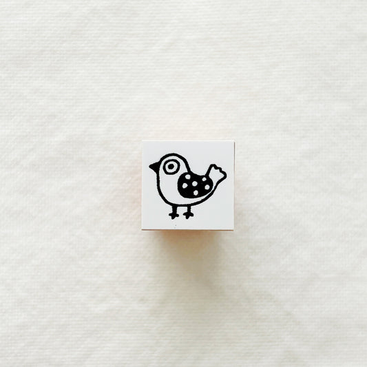 Small square rubber stamp block with a black and white bird design on a white textured background