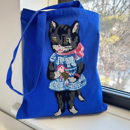 A tote bag with a black cat design on a blue background