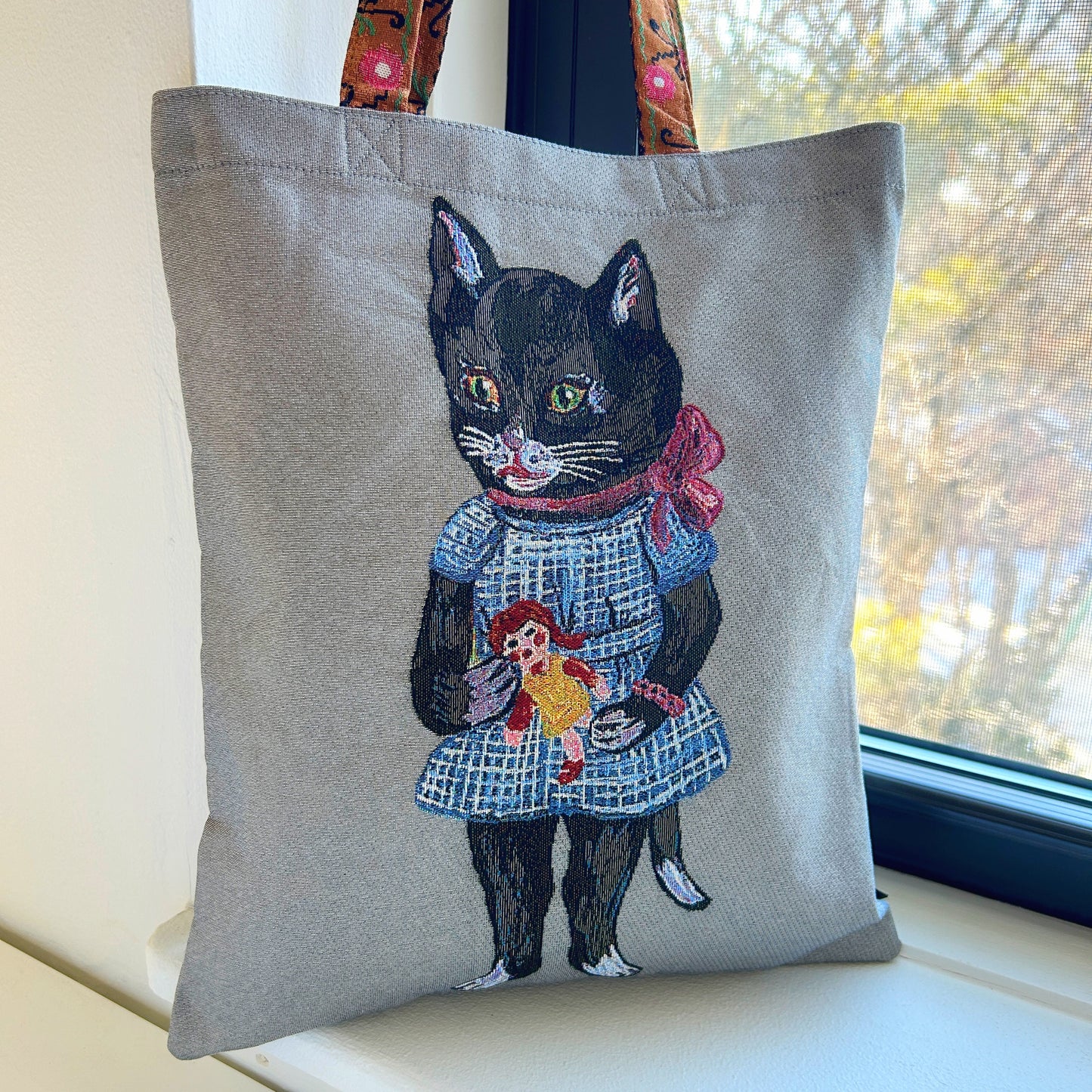 Tote bag with a black cat holding a doll design against a grey background