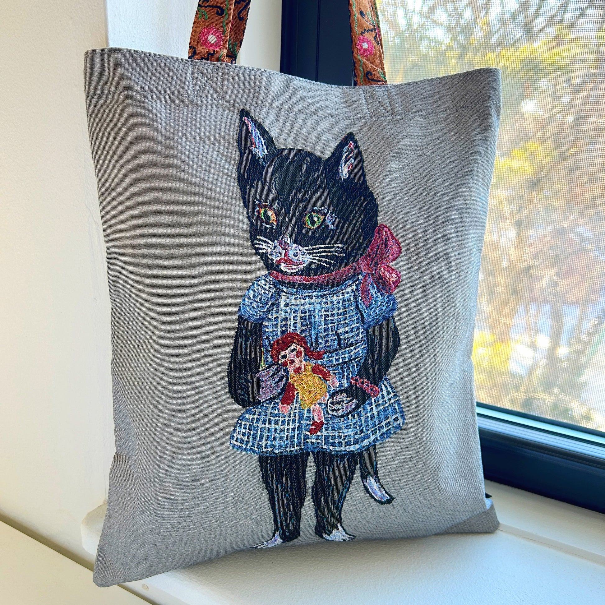 Tote bag with a black cat holding a doll design against a grey background