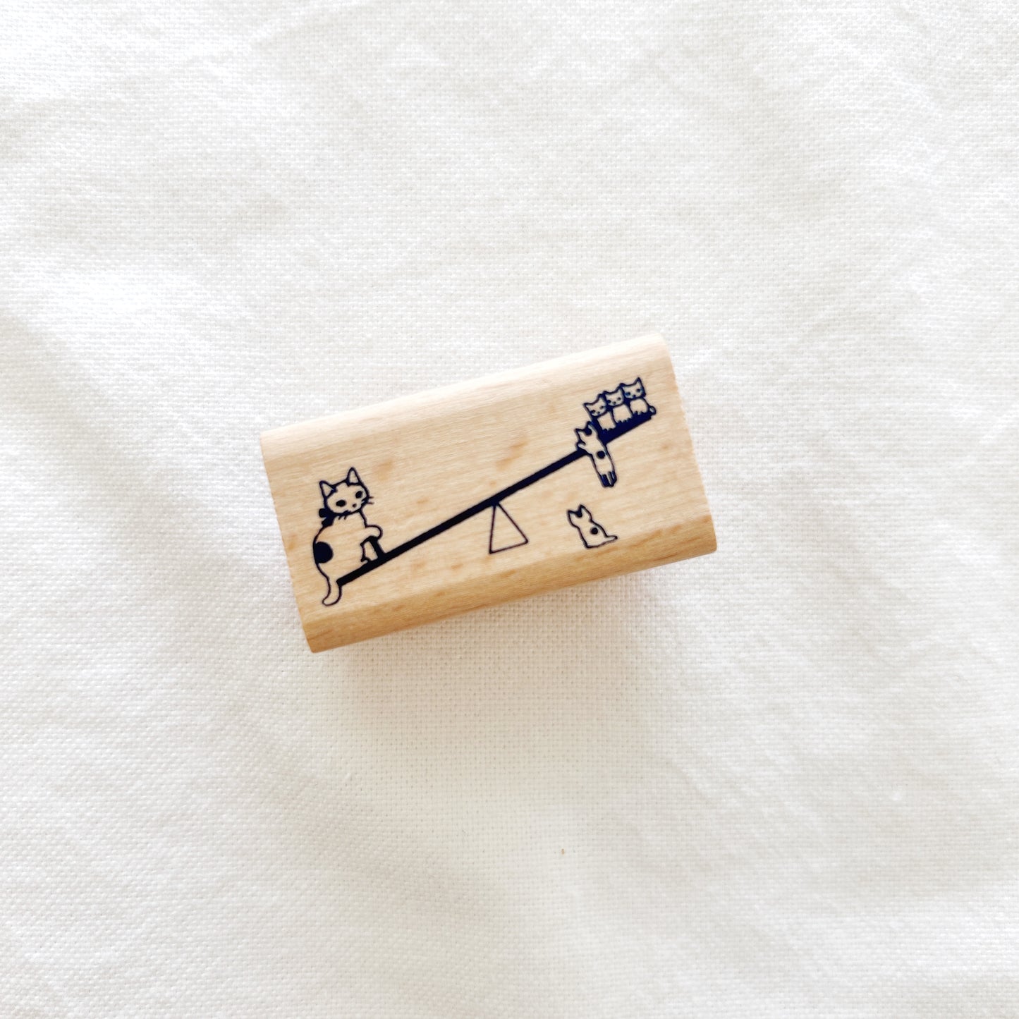 Wooden stamp of a mother cat and her kittens playing on a seesaw
