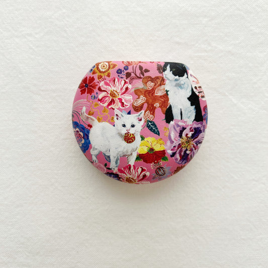 A round travel case with mirror.  Designs include cats and flowers